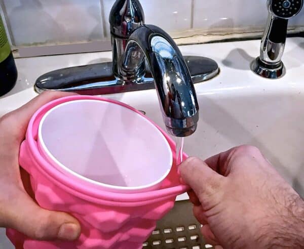 A person fills The Ultimate Mini Ice Cube Maker Pink Silicone Bucket Ice Mold and Storage Bin Portable 2 in 1 Ice Cube Maker with water from a kitchen sink faucet to use in The Ultimate Mini Ice Cube Maker.
