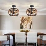 Two Modern Semi Flush Mount Ceiling Light Crystal Ceiling Lights with 12 Inch Round Metal and Crystal Shades Matte Black hang above a wooden dining table with six white chairs in a neutrally decorated room with an abstract painting on the wall.