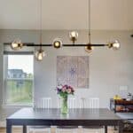 Modern dining room with a black table and white chairs under a Mid-Century Light Pendant Lighting Mid-Century Glass Globes Chandelier Black, featuring a wall tapestry and a vase of flowers.